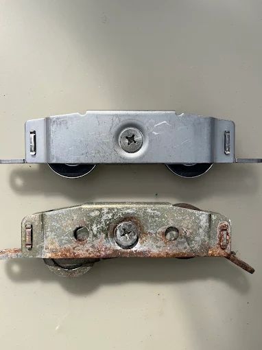 Worn, rusted sliding door rollers next to brand-new stainless replacement rollers
