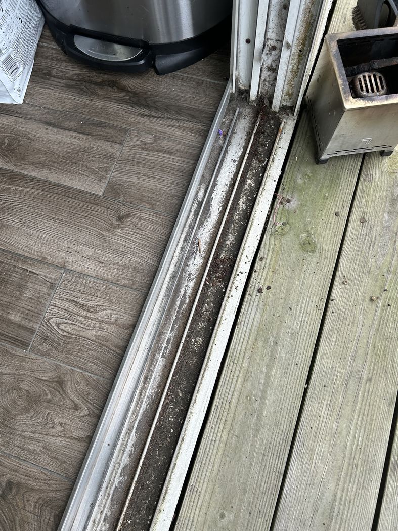 Worn and pitted aluminum sliding door track full of debris on a patio